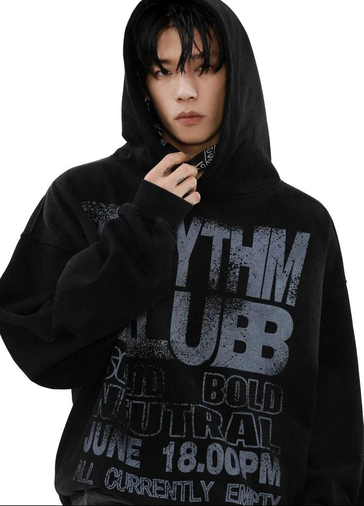 フードをかぶった黒いキャンバス フーディーを着た人物が白い背景に立っています。フーディーには、「RHYTHM KLUBB」のほか、「BOLD」および「June 18:00 PM」という太字のグランジ スタイルの文字が書かれています。人物は顔の近くに手を置いています。.